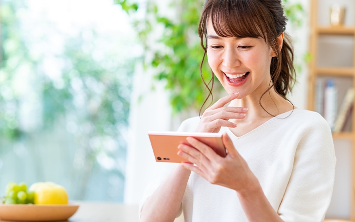 スマートフォンの画面を見ながら笑っている女性の画像。