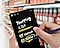 Primer plano de una persona en un supermercado sosteniendo un teléfono y un S Pen. La pantalla del teléfono muestra el texto escrito a mano “Lista de compras” con una lista con los artículos “zanahoria” y “manzana”.
