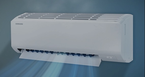 Un primer plano de un aire acondicionado Samsung montado en la pared se acerca lentamente. Su pantalla digital muestra 23°C. El aire es aspirado desde la entrada superior y dispersado desde la hoja inferior.