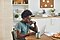 Un hombre está sentado en una mesa en su cocina con una computadora portátil Galaxy Book Pro de color gris claro. Está usando un par de Galaxy Buds Pro negros.