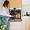 A woman slides a tray of muffins into a switched-on oven.