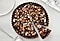 Chocolate tart topped with mashed nuts on it is on a white table.