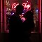 Silhouette photography of a couple standing in front of a neon coffee shop light, the scene is dark but you can make out their outline