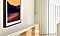 Inside a brightly lit living room, The Frame TV is seen from a side closeup and is hung using its wall mount option. There is an image of a sunset mountain scene on the screen.
