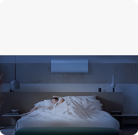 A person sleeps peacefully in a dark room, lying under a Samsung wall-mounted air conditioner.