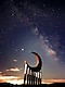 Sculpture of a moon, supported by columns against a starry night sky during sunset