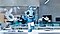 A whimsical looking blue alien dancing happily on top of a lab desk. As if making air quotes, the alien is holding up both hands in a way that mimics the antennae.