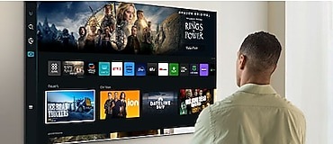شخص يقف أمام تلفزيون Smart TV ويتنقل عبر عدد وفير من خيارات المحتوى وخدمة OTT.