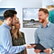 For buying a new TV, a man and woman are talking with a male sales representative about TV features in a TV show room.