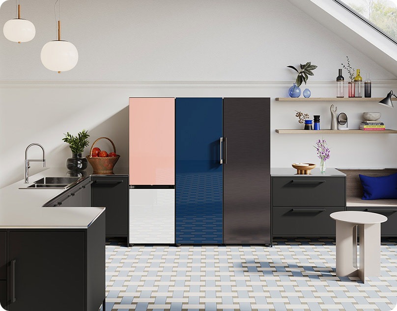 Trīs Bespoke ledusskapji novietoti blakus viens otram blakus gaišā, atvērta tipa virtuvē. Redzams Bespoke divdurvju ledusskapis, kuram augšējā daļa ir rozā, bet apakšējā – baltā krāsā, viendurvju Bespoke ledusskapis tumši zilā krāsā un viendurvju  Bespoke ledusskapis melnā krāsā.