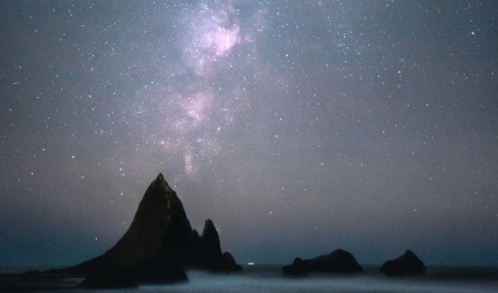 Una formación rocosa en una playa frente a un cielo estrellado nocturno.