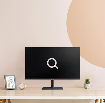 Un fondo rosa beige. Un monitor en la parte superior de la mesa de madera con un icono de búsqueda grande.
