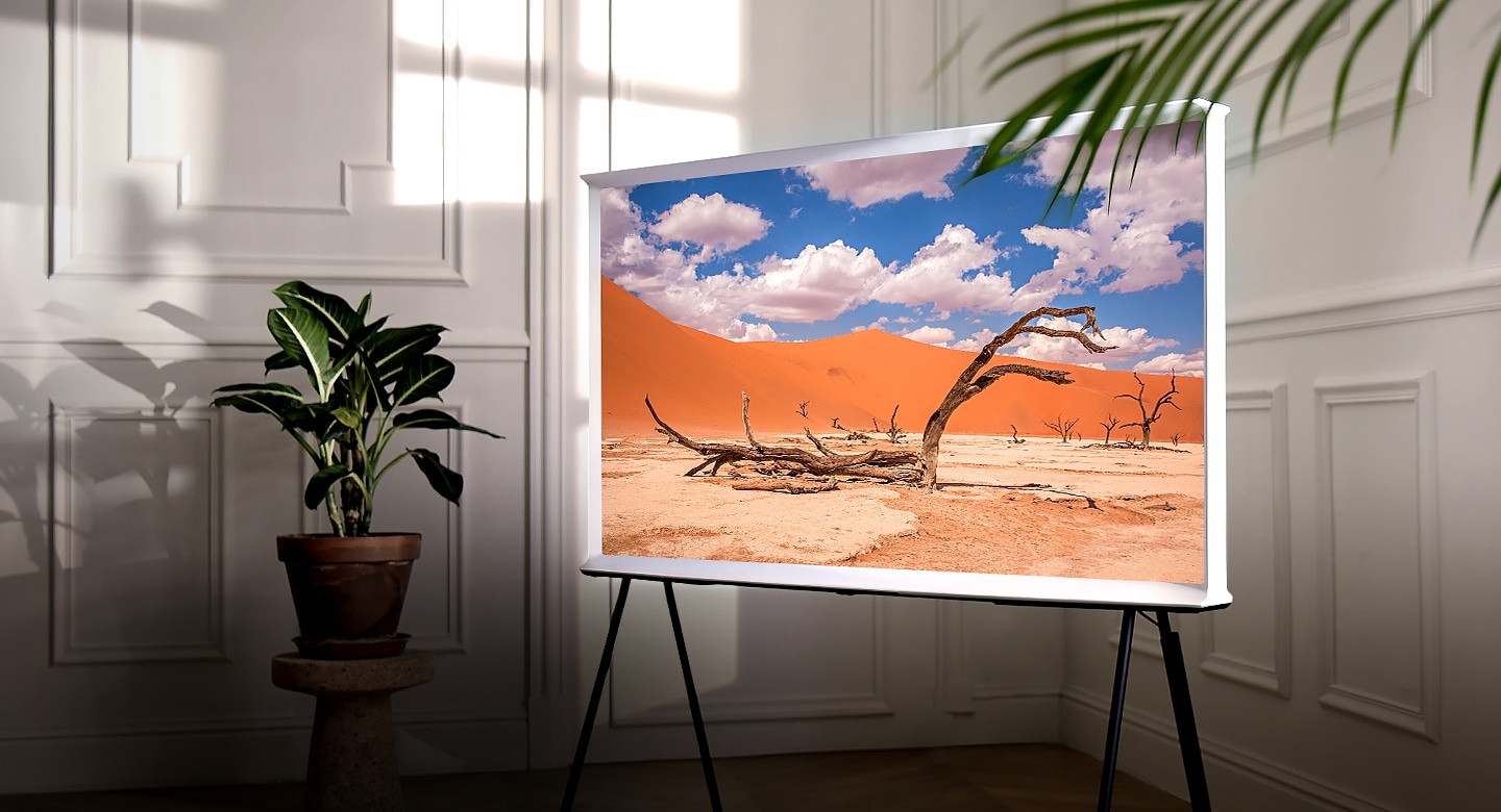 The Serif Cloud White en un mueble de televisión en la esquina de una habitación, con una hermosa imagen de un desierto con cielos azules y nubes blancas.