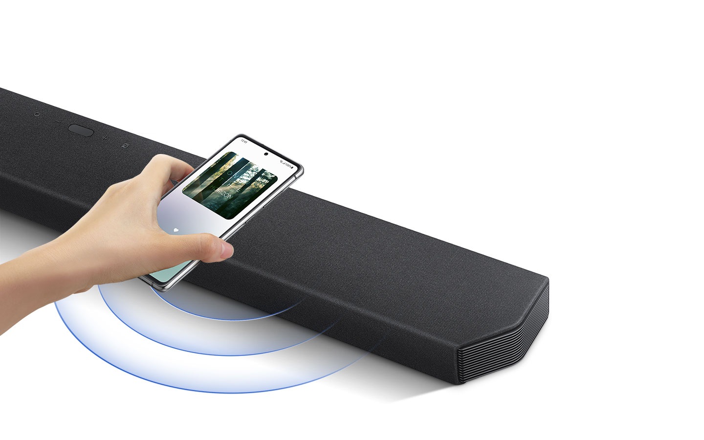 A hand taps a smartphone with the Samsung music app on-screen on the soundbar.