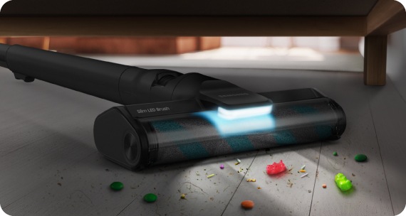 A cat is lying on the living room floor and a Samsung Cordless vacuums is cleaning the pet's fur in front of it.