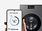 In front of a washing machine, a hand holds a Galaxy smartphone displaying the AI energy mode SmartThings app UI.