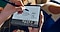 Someone holding  a Galaxy Z Fold3 5G while using the S Pen Fold Edition to make handwritten notes and sketches on a whiteboard that's on the screen. On the bottom of the screen there are thumbnails of the participants of a video chat that is taking place on the device at the same time.