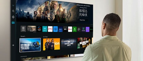 Une personne debout devant une Smart TV parcourt une multitude de contenus et d’options OTT. Une personne debout devant une Smart TV parcourt une multitude de contenus et d’options OTT.