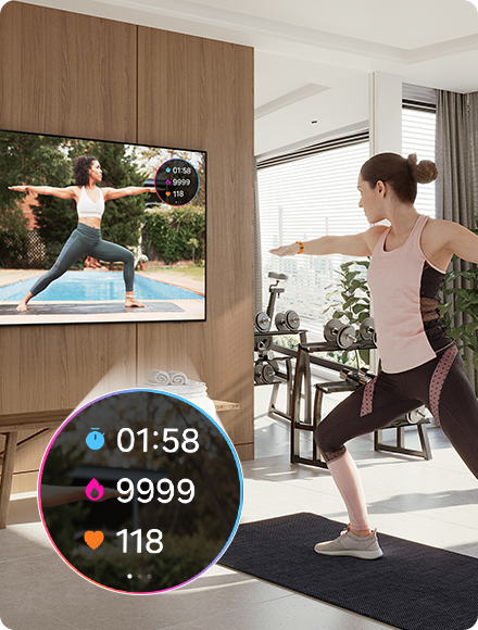 Une femme fait du yoga tout en regardant un coach à la télévision. La télévision affiche également les statistiques d’exercice 01:58, 9 999, 118 de la Galaxy Watch connectée.