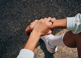 Twee handen van een persoon in een sportoutfit, zittend op de stoep. Een zwarte Galaxy Ring om de linkerhand.