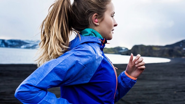 Een vrouw die aan het hardlopen is bij een meer, met roze Galaxy Buds in haar oren.
