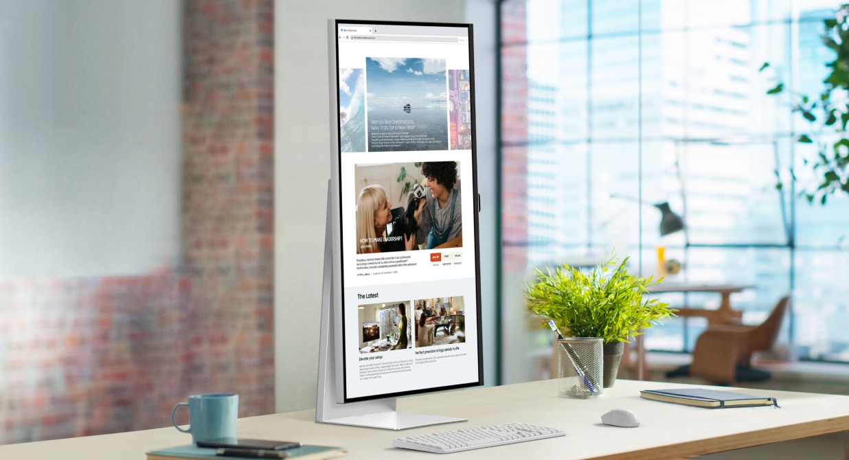 We zien een Samsung ViewFinity-monitor op een bureau in een licht en modern kantoor staan. Het scherm staat in portretmodus en er wordt een webpagina getoond. Het ergonomische design is in hoogte verstelbaar en biedt draai- en kantelopties voor een optimale kijkhoek.