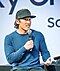 Jimmy Chin draagt een honkbalpetje en een blauwe sweater en spreekt op een podium tijdens de Creators Talk in de Creator Lounge