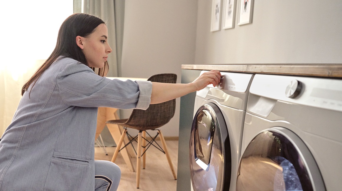 Een vrouw in een blauwe jas bedient de Samsung wasmachine.