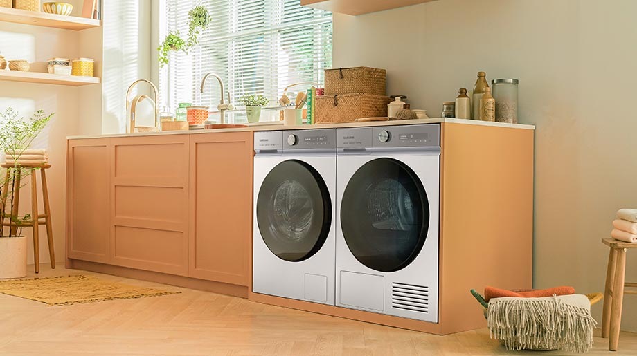 En svart Bespoke AI™ vaskemaskin og tørketrommel ved siden av hverandre ved siden av et treskap i et rom med beige vegger og et fargerikt flislagt gulv.