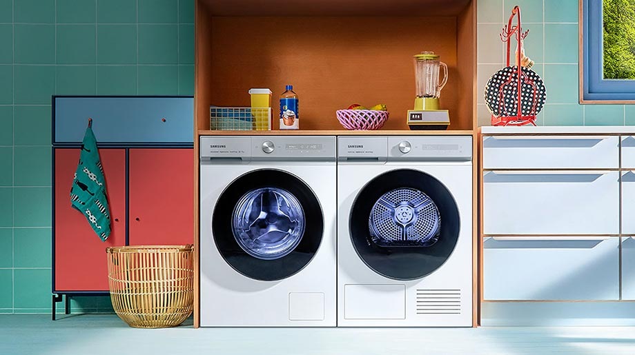 En hvit Bespoke AI™ vaskemaskin og tørketrommel stablet og bygd inn i et grønt skap på et elegant kjøkken.