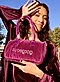 A woman in a purple jacket and dress shows off her purple purse on a neighborhood street.