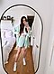 A woman in green pajamas takes a mirror selfie in her bedroom.