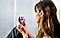 A side-profile view of a lady sitting, she has the Galaxy Buds Plus in her ear and is holding the Galaxy Z Flip phone in both hands in front of her