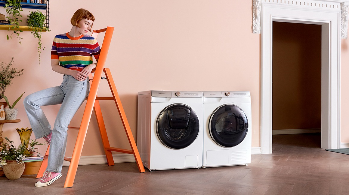 A woman who is leaning on the ladder is watching the Samsung washing machine and dryer.
