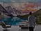 Un hombre con una taza de café delante de un televisor de gran tamaño que muestra un paisaje al aire libre con una cadena montañosa y un lago. La imagen se expande más allá de la pantalla.