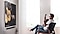 A man sits in a living room chair playing an acoustic guitar while watching a screen showing a guitar tutorial from Neo QLED 8K