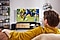 Młody mężczyzna ogląda mecz w nowocześnie urządzonym salonie. Na szafce, pod telewiorem, ustawiony jest soundbar Samsung Q-serii.