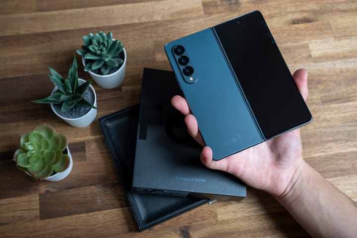 Wyjęty z pudełka i trzymany w dłoni na tle blatu smartfon Samsung Galaxy Z Fold4. Obok stoją kwiatki.
