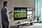 Mężczyzna ze smartfonem w ręku stojący przed ekranem telewizora Samsung Smart TV.