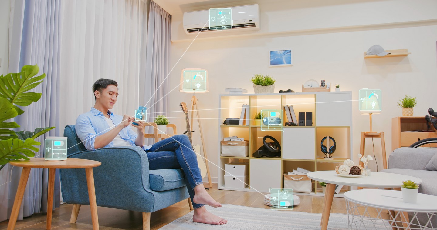 Mężczyzna siedzący w fotelu ze smartfonem w ręku, zarządzający inteligentnymi urządzeniami w smart home.