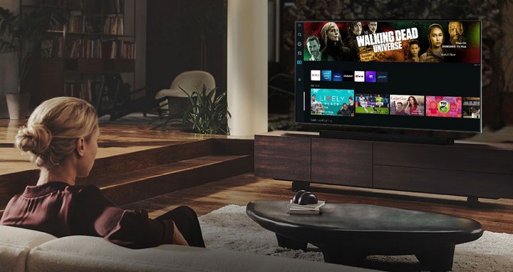 Siedząca na sofie kobieta przed ekranem telewizora Samsung Smart TV.