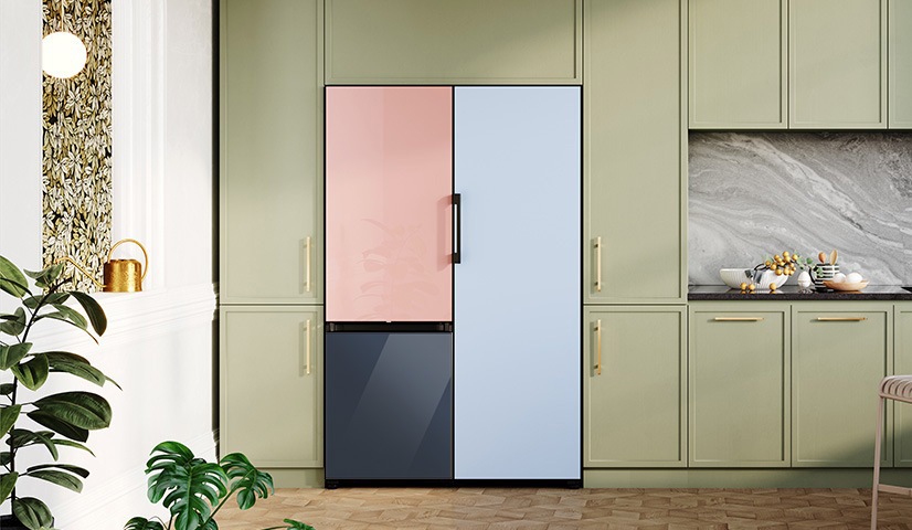 A green kitchen is shown with a multicoloured Bespoke Fridge in the middle. Plants are scattered to the left.