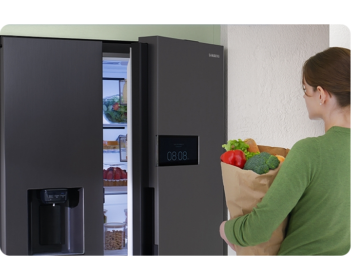 Kobieta stojąca przed otwartą lodówką Bespoke AI z torbą jedzenia