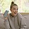 Millie Bobby Brown sitting on a couch, holding up an Aura Glow Galaxy Note10