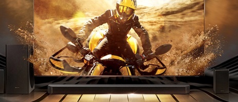 يوجد أسفل شاشة التلفزيون جهاز صوت Q950T مع مضخمات الصوت أسفله. يظهر على شاشة التلفزيون منظر أمامي لشخص يركب دراجة ترابية. لمحاكاة الصوت الاندماجي لجهاز الصوت ومكبر صوت التلفزيون، تبدو الأوساخ المتناثرة من الدراجة الترابية وكأنها تتطاير من على جوانب الشاشة إلى غرفة المشاهد.