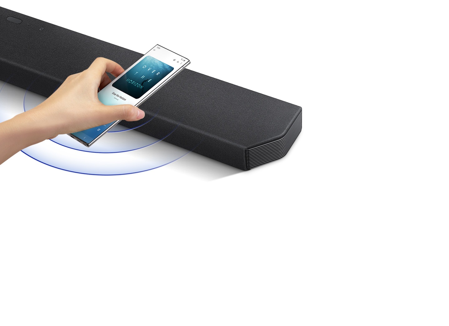 Uma mão toca num smartphone com a aplicação de música Samsung no ecrã na soundbar.