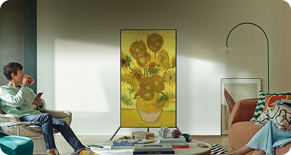 Um homem vê televisao com com um Suporte Studio Stand Rotativo Automático. A TV apresenta uma pintura de flores no modo vertical.