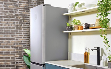 Um frigorífico Samsung RB7300T está colocado ao lado de bancadas de cozinha de cor azul cadete e parece que a cozinha tem uma decoração minimalista.