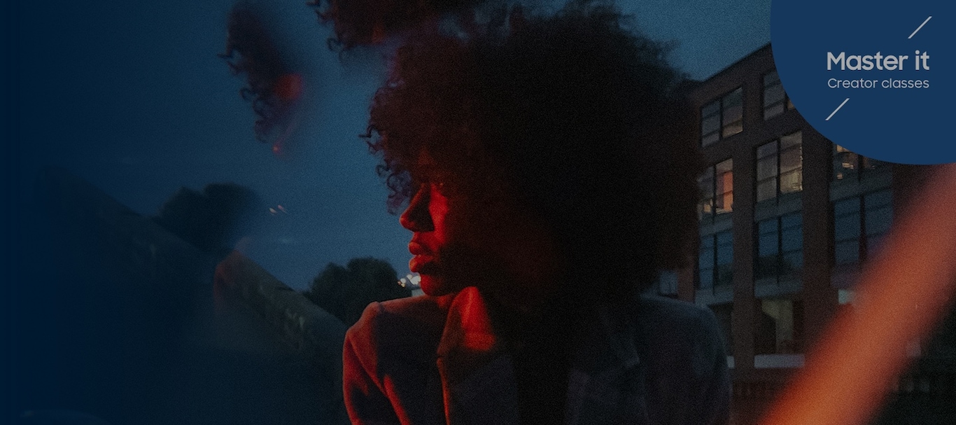 Una mujer con una chaqueta que mira hacia la izquierda, sutilmente iluminada por una luz roja frente a un cielo azul. Master it Creator classes. Capturado #withGalaxy S22 Ultra1