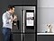 A man drinks a glass of water in the kitchen while checking on his sleeping daughter from the Family Hub screen connected to SmartThings.